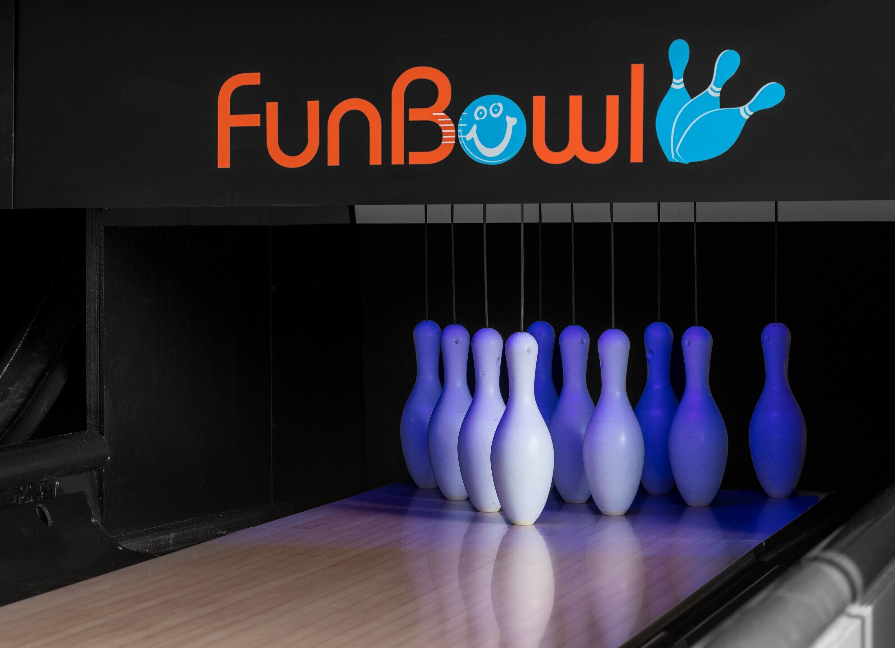 Een bowlingbaan met een bord waarop 'FunBowl' staat en een rij bowlingpinnen.