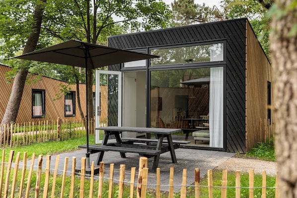 A modern outdoor dining area with a picnic table and umbrella, surrounded by a wooden fence and trees.