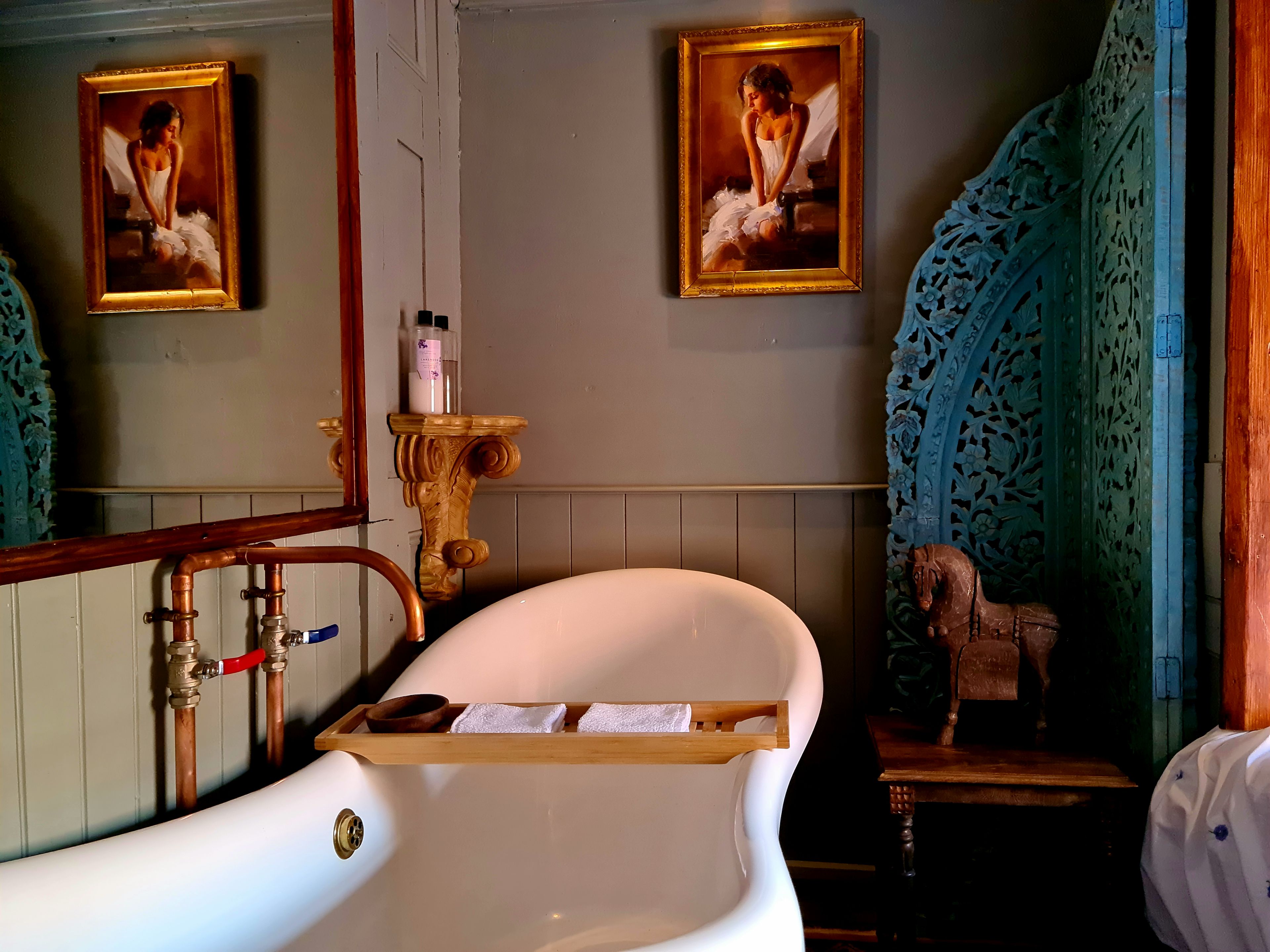 A bathroom with a white bathtub, wooden towel rack, and two framed paintings on the wall.