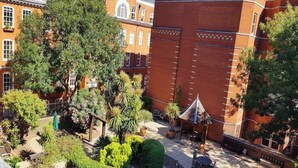 Une cour avec un bâtiment en briques, un kiosque et diverses plantes en pot.