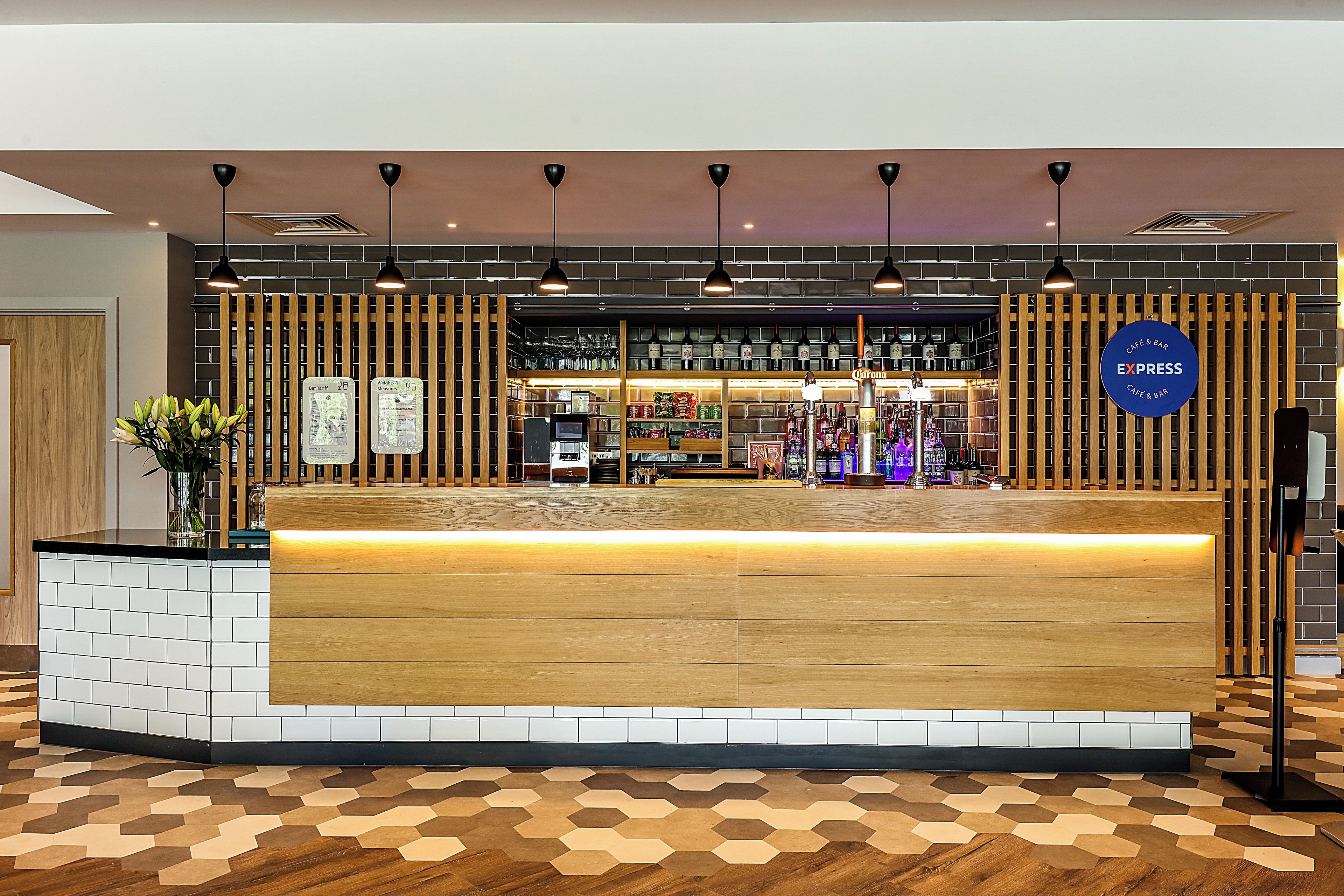 A reception desk with a wooden counter, a tiled floor, and a wall with shelves of bottles and a sign for 'Café & Bar Express'.