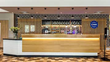 A reception desk with a wooden counter, a tiled floor, and a wall with shelves of bottles and a sign for 'Café & Bar Express'.