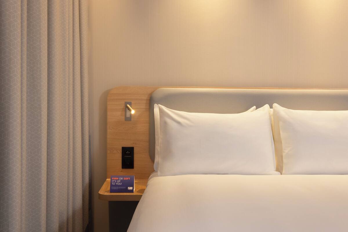 A hotel room with a wooden headboard, a bedside table with a lamp, and a sign indicating room temperature control.