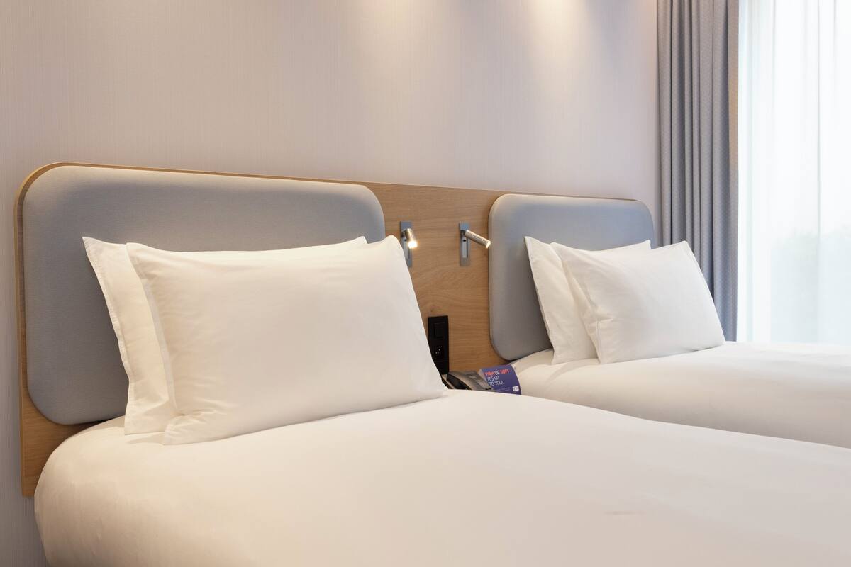 A hotel room with two beds, each with white bedding and a wooden headboard.