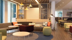 A modern lounge area with seating arrangements, pendant lighting, and a large window providing natural light. - Holiday Inn Express Brussels Airport by IHG (Machelen)
