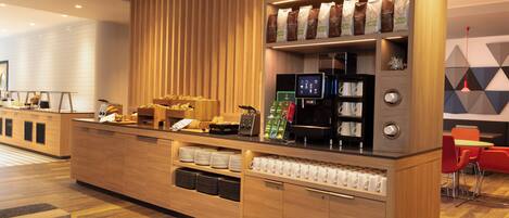 A modern coffee station with a wooden counter, coffee machines, and a variety of coffee bags.