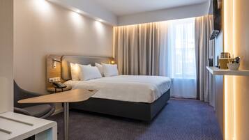 Een hotelkamer met een bed, nachtkastje, bureau, stoel en een aan de muur bevestigde televisie.