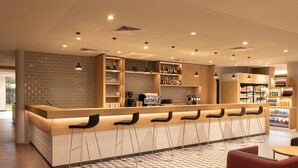 A modern bar area with a long counter, multiple stools, and shelves stocked with bottles. - Holiday Inn Express Brussels Airport by IHG (Machelen)