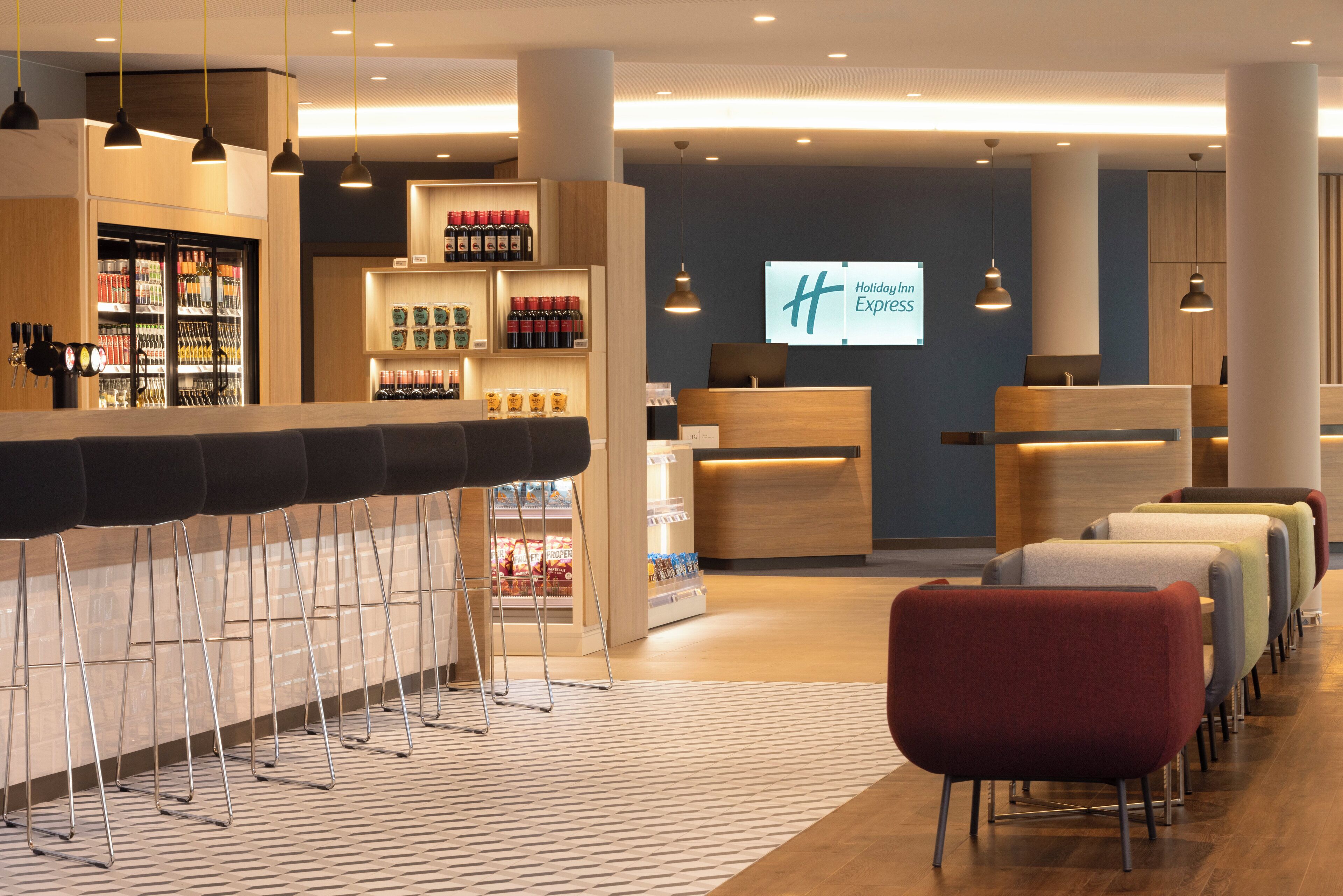 A hotel lobby with a reception desk, a minibar, and a seating area with chairs.