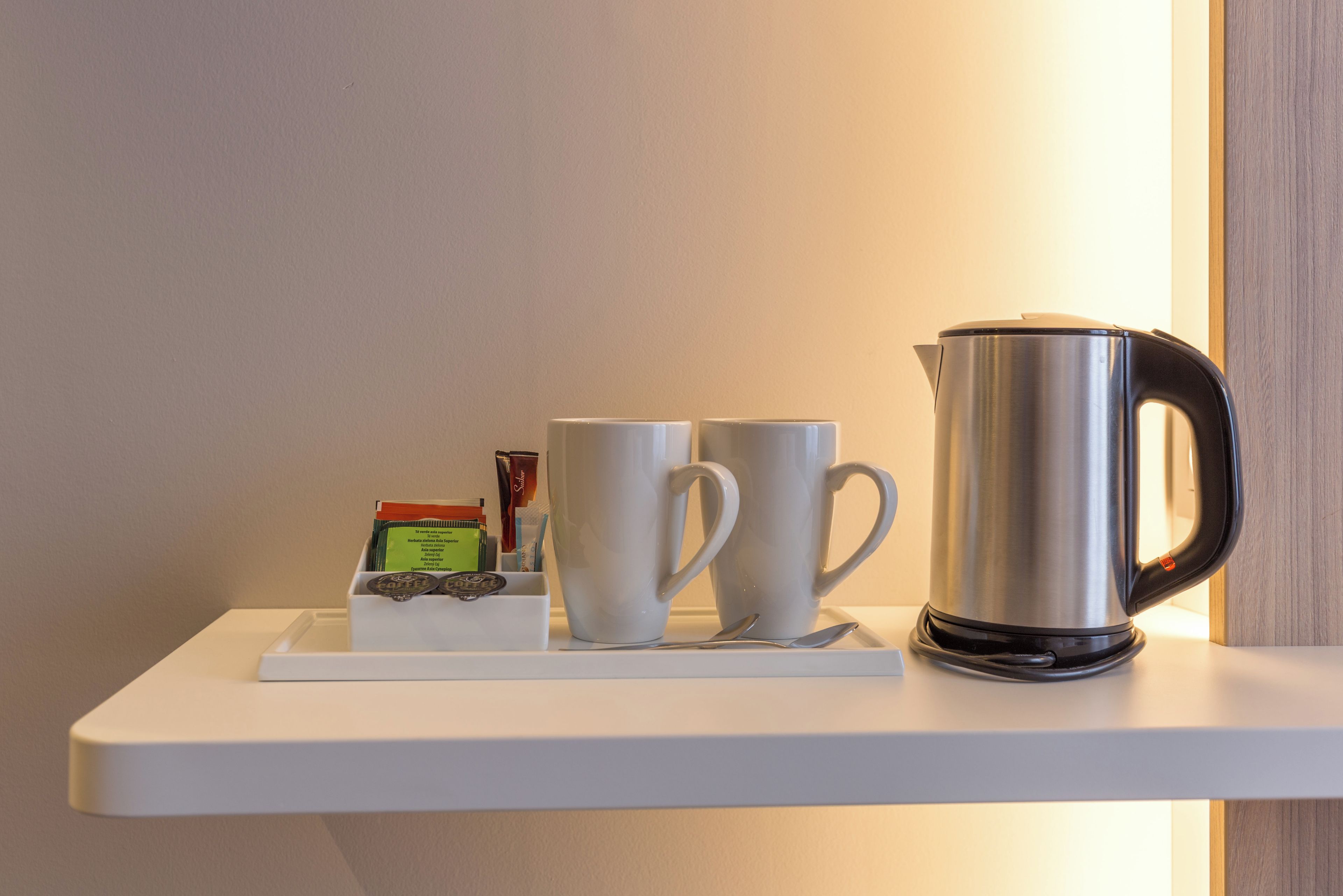 A white shelf with a stainless steel electric kettle, two white cups, and a box of coffee creamer.