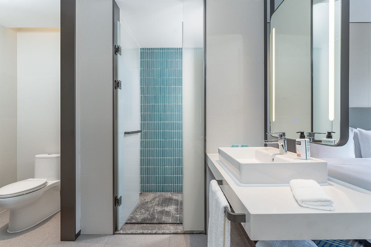 A modern bathroom with a white toilet, a glass shower enclosure, a blue-tiled shower area, a white sink with a mirror, and a white towel on the counter.