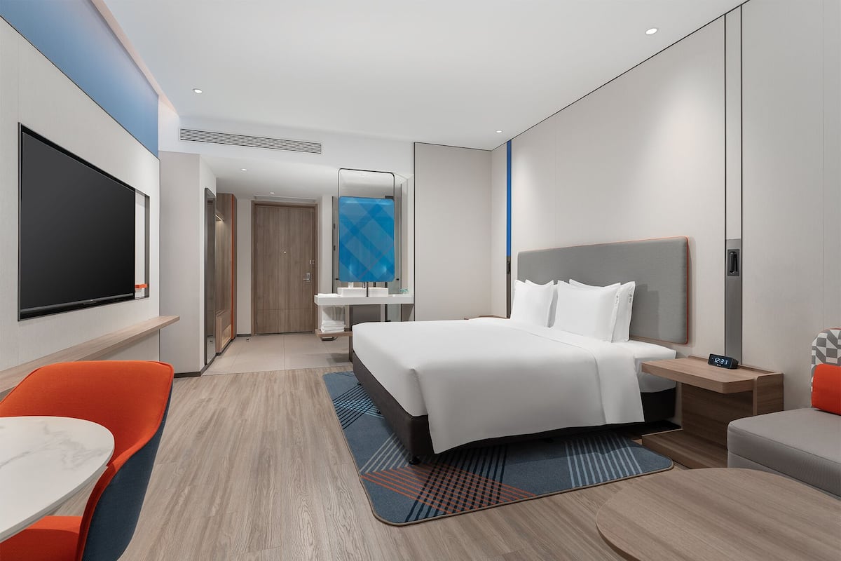 A modern hotel room with a large bed, a desk, a chair, a TV, and a bathroom.