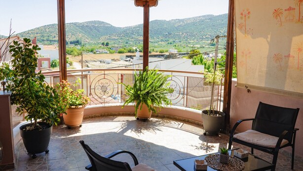 Un espacio al aire libre cubierto con vistas a un paisaje montañoso. Hay plantas en macetas, una silla y una mesa.