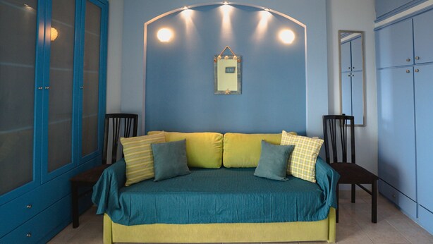 A bedroom with a bed, a chair, a wardrobe, and a mirror on the wall. - Lilly s Seaview Studio (South Pelion)