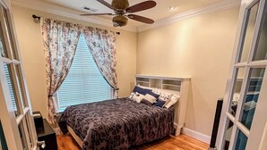 Ein Schlafzimmer mit Bett, Holzboden, Deckenventilator und einem Fenster mit Vorhängen.
