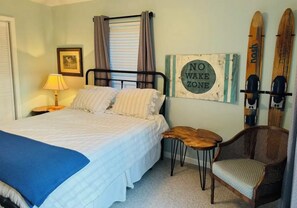 A neatly arranged bedroom with a bed, a chair, a small table, and a wall-mounted sign.