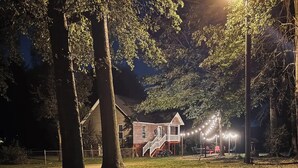 A house with a porch and a staircase leading to a deck, surrounded by trees and string lights. - Relax & enjoy the river view, 5 min to Huntsville (Laceys Spring)