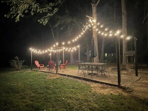 An outdoor patio area with string lights, a swing, and a table with chairs.