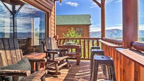 Un ponte di legno con mobili da esterno, vista sulle montagne e una baita sullo sfondo.