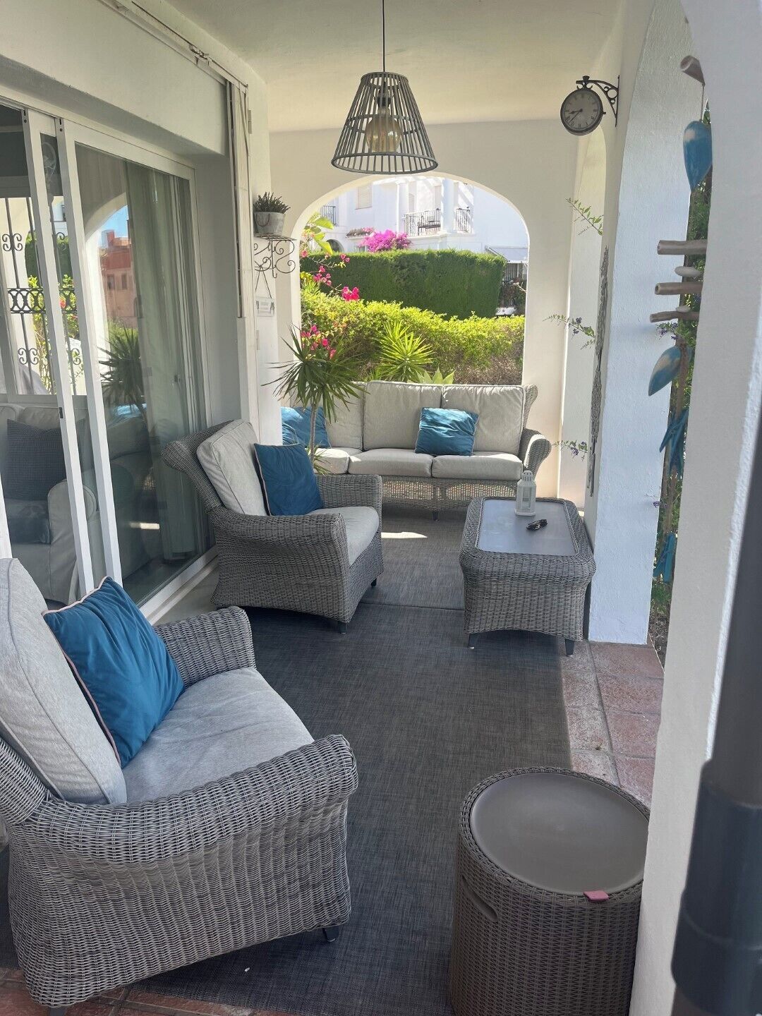 Un área de patio techada con mobiliario de mimbre, una mesa y una lámpara colgante.