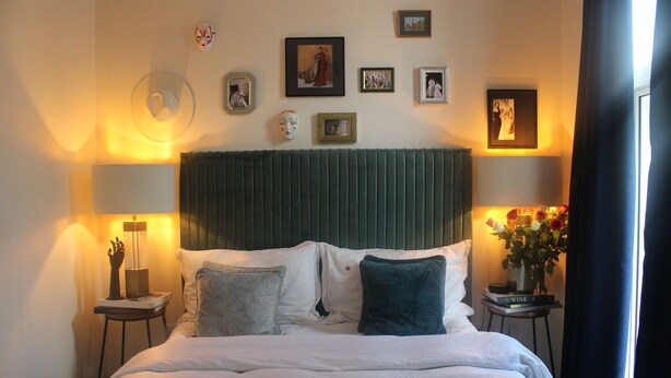 A neatly made bed with a green headboard, two bedside tables with lamps, and framed pictures on the wall. - London Gem - Chic Apartment Retreat (London)