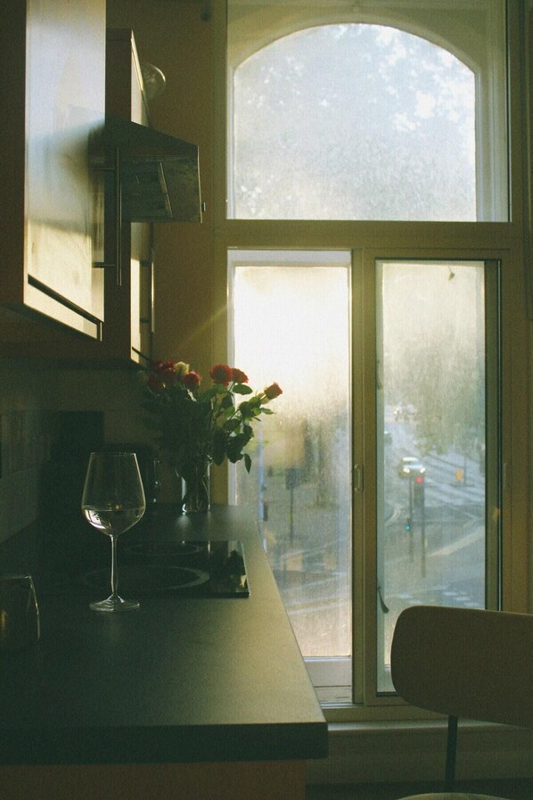 Ett kök med ett stort fönster, en vas med blommor och ett glas vatten på bänkskivan.
