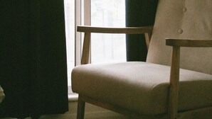 A room with a single chair near a sliding glass door, curtains partially drawn, and a view of a building outside. - London Gem - Chic Apartment Retreat (London)
