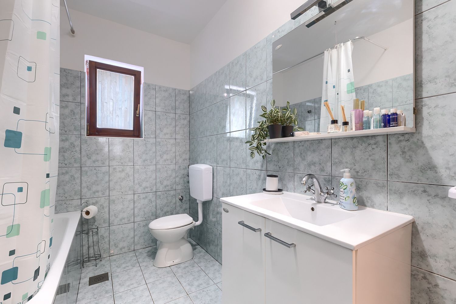 A bathroom with a toilet, sink, mirror, and a shelf with toiletries.