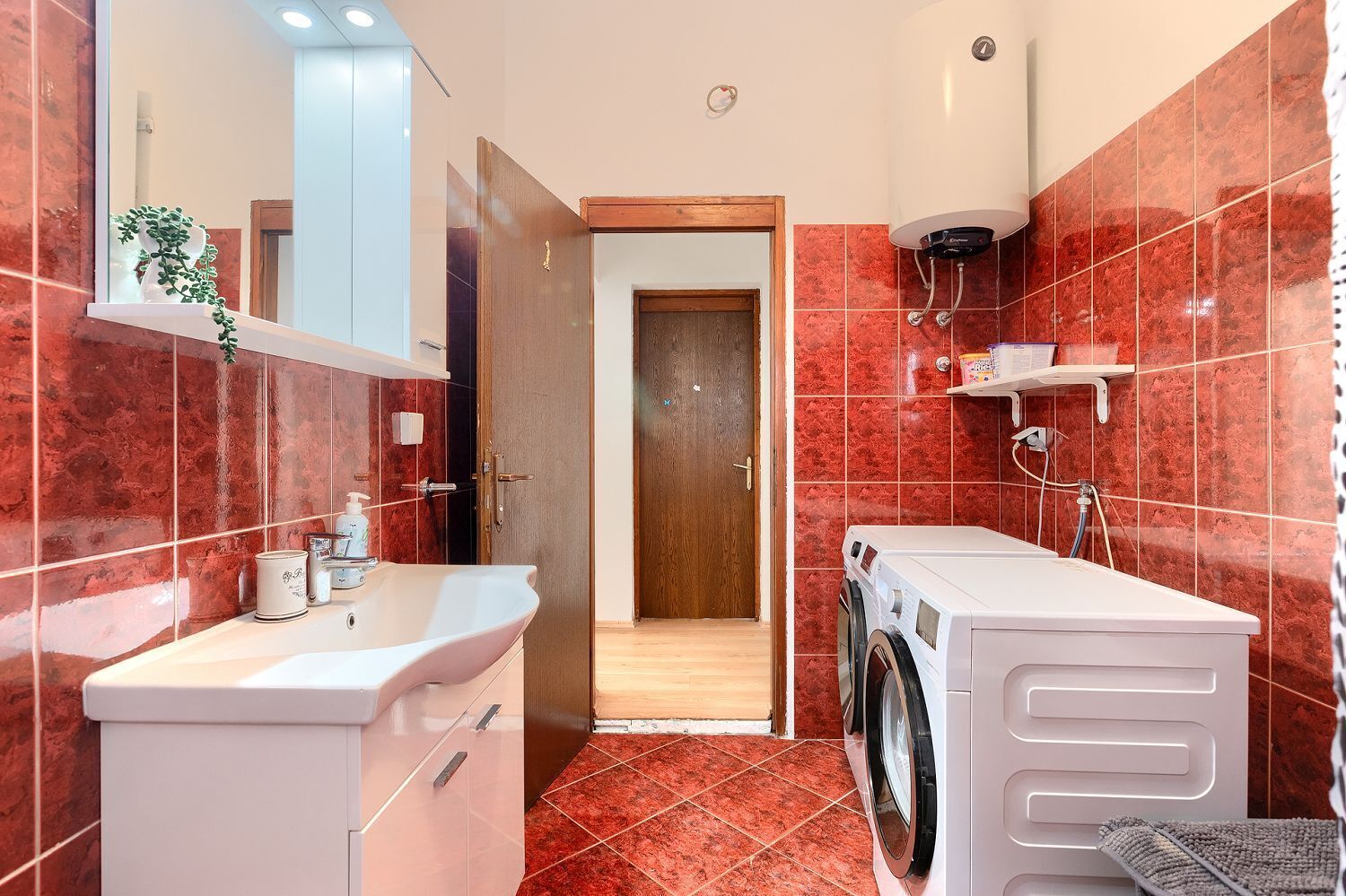 A modern bathroom with a sink, mirror, and washing machine.