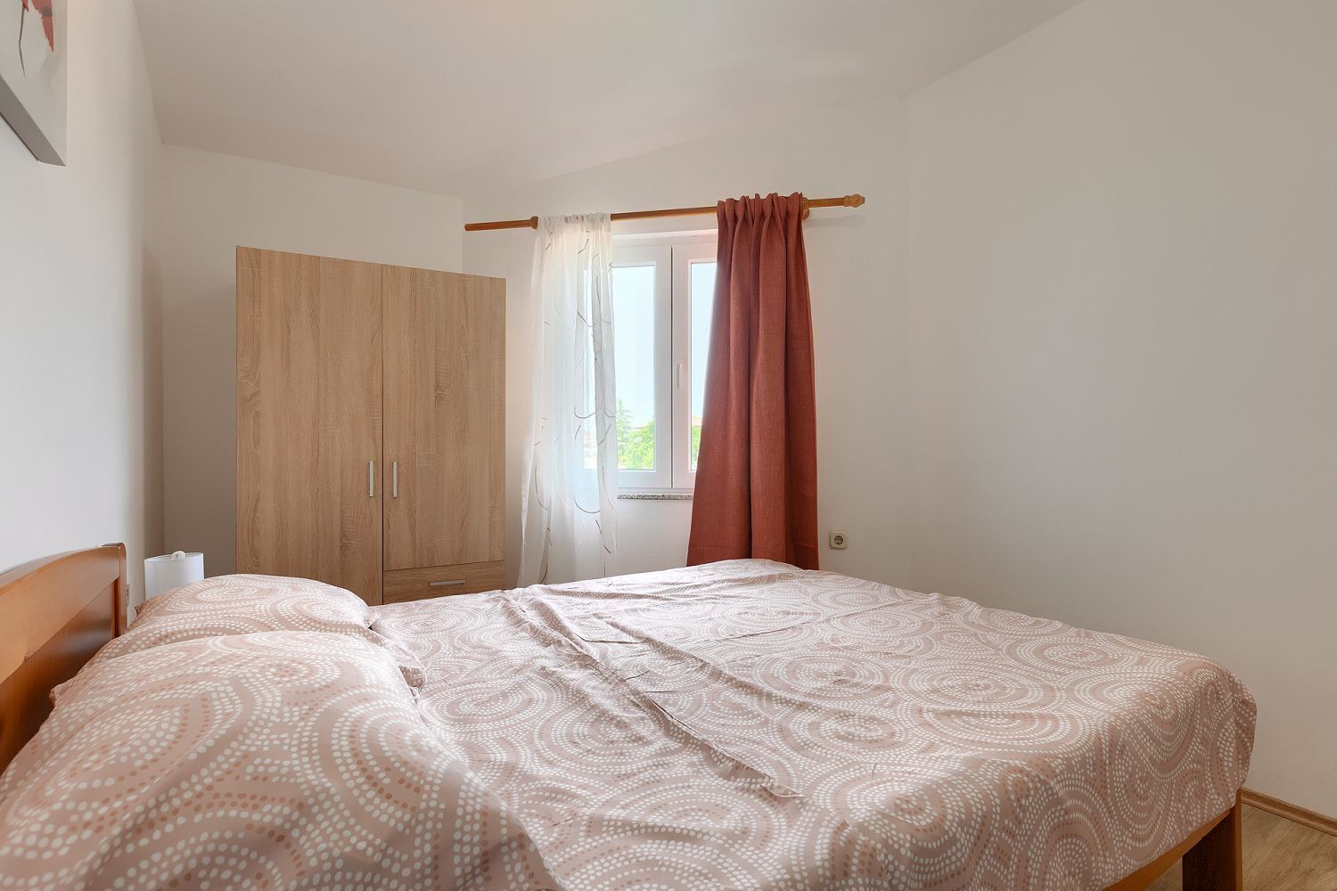 A bedroom with a bed, a wardrobe, and a window with curtains.