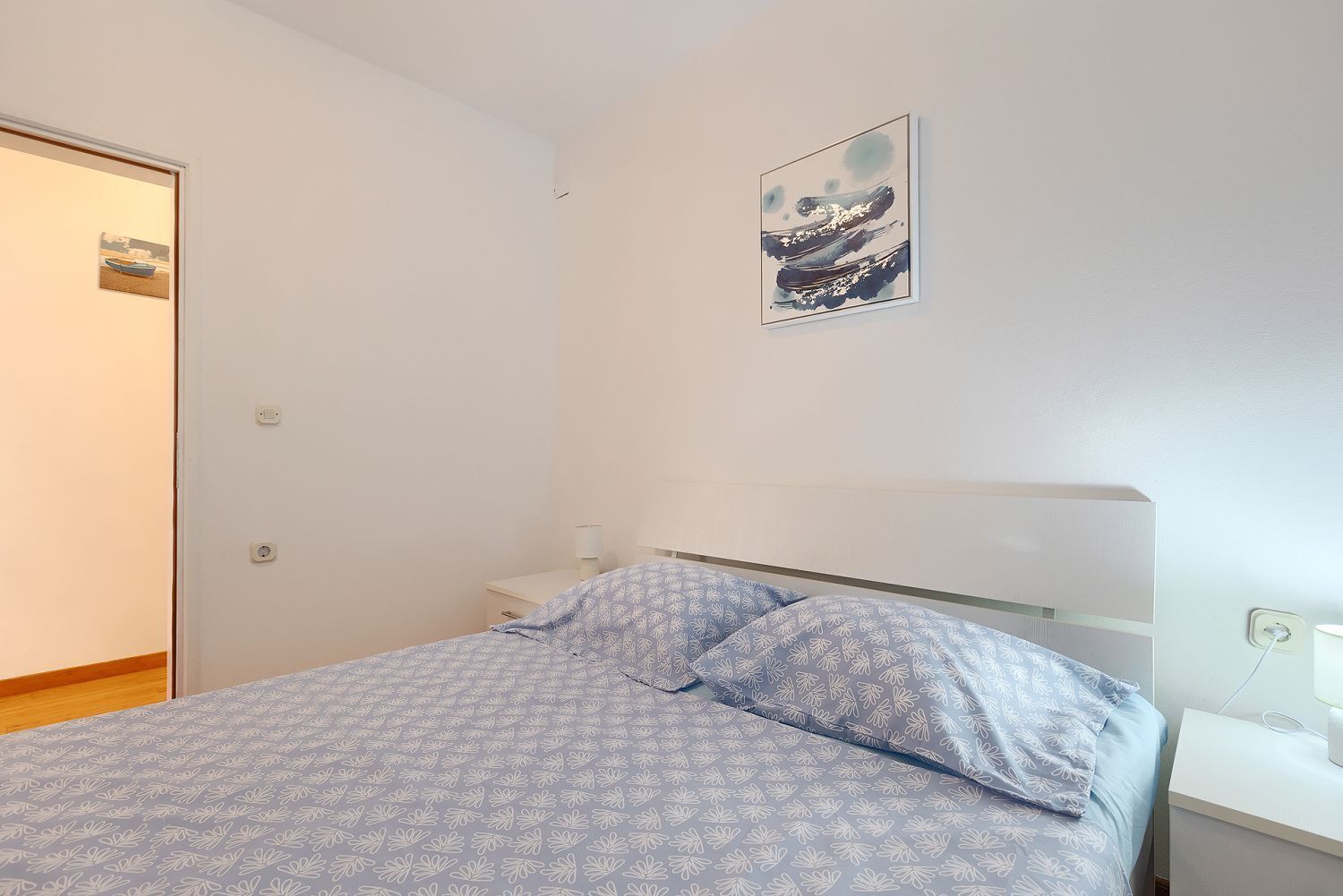 Un dormitorio con cama, mesita de noche, un cuadro colgado en la pared y una puerta.