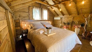 Una habitación acogedora de madera con una cama, una mesita de noche, una lámpara y una planta en maceta.