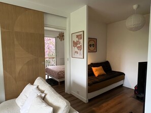 Una habitación con sofá, cama, televisión y balcón con vista a árboles.