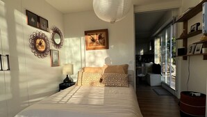 A bedroom with a bed, a hanging light fixture, a chair, and a view of the outside.