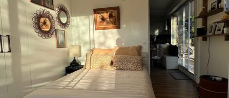 Un dormitorio con cama, lámpara colgante, silla y vistas al exterior.