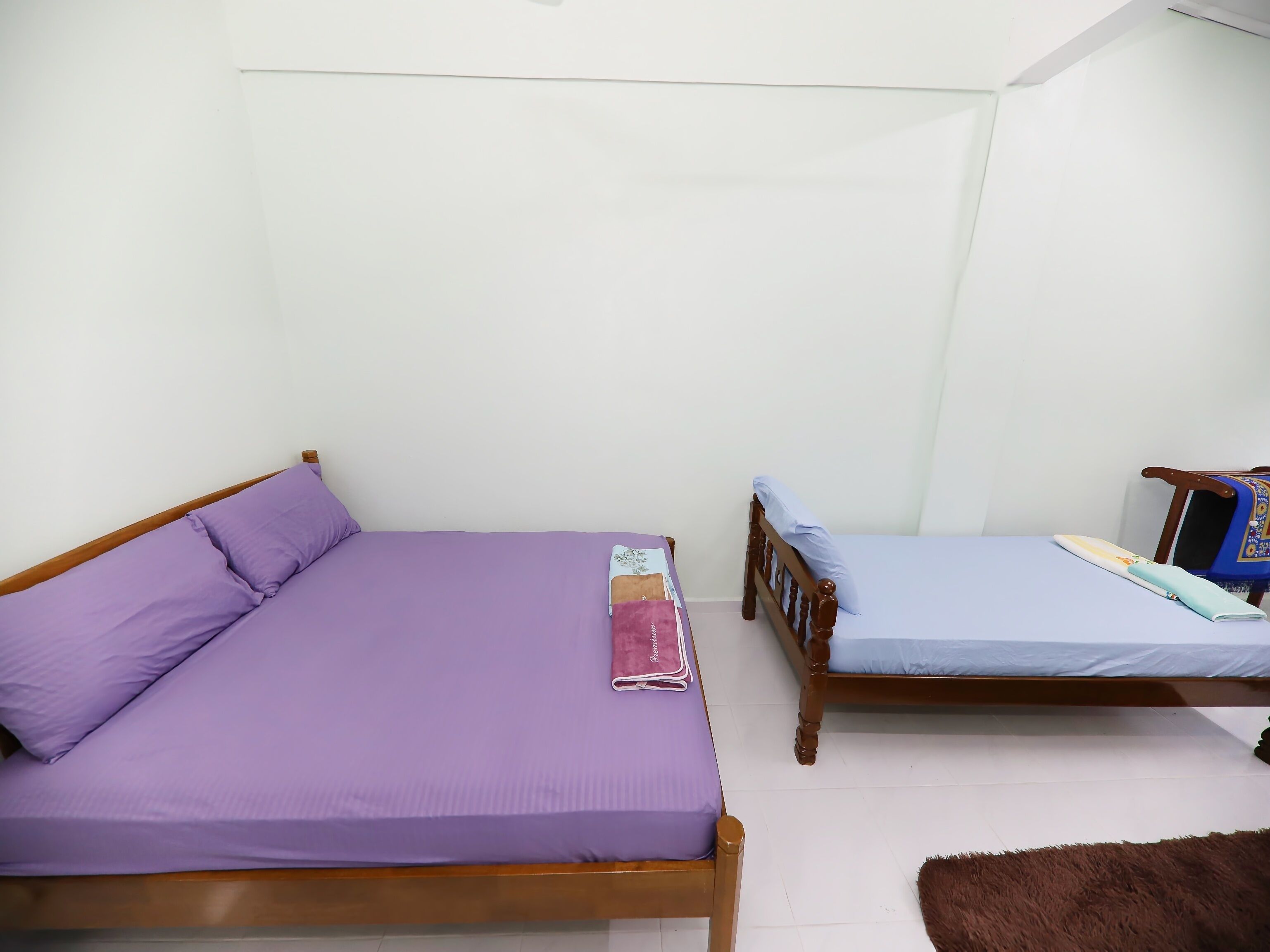 Two single beds with wooden frames and purple bedding, a small table with a blue cloth, and a brown furry rug on the floor.