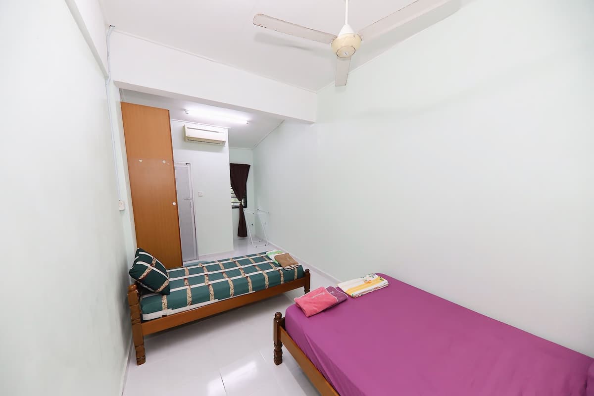 A small, clean room with two single beds, a ceiling fan, and an air conditioning unit.