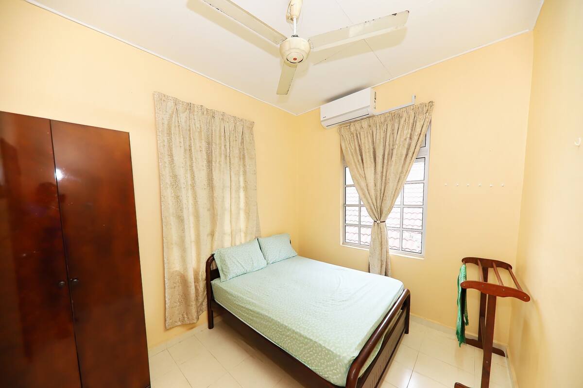 A bedroom with a bed, a wardrobe, a ceiling fan, an air conditioning unit, and a window with curtains.
