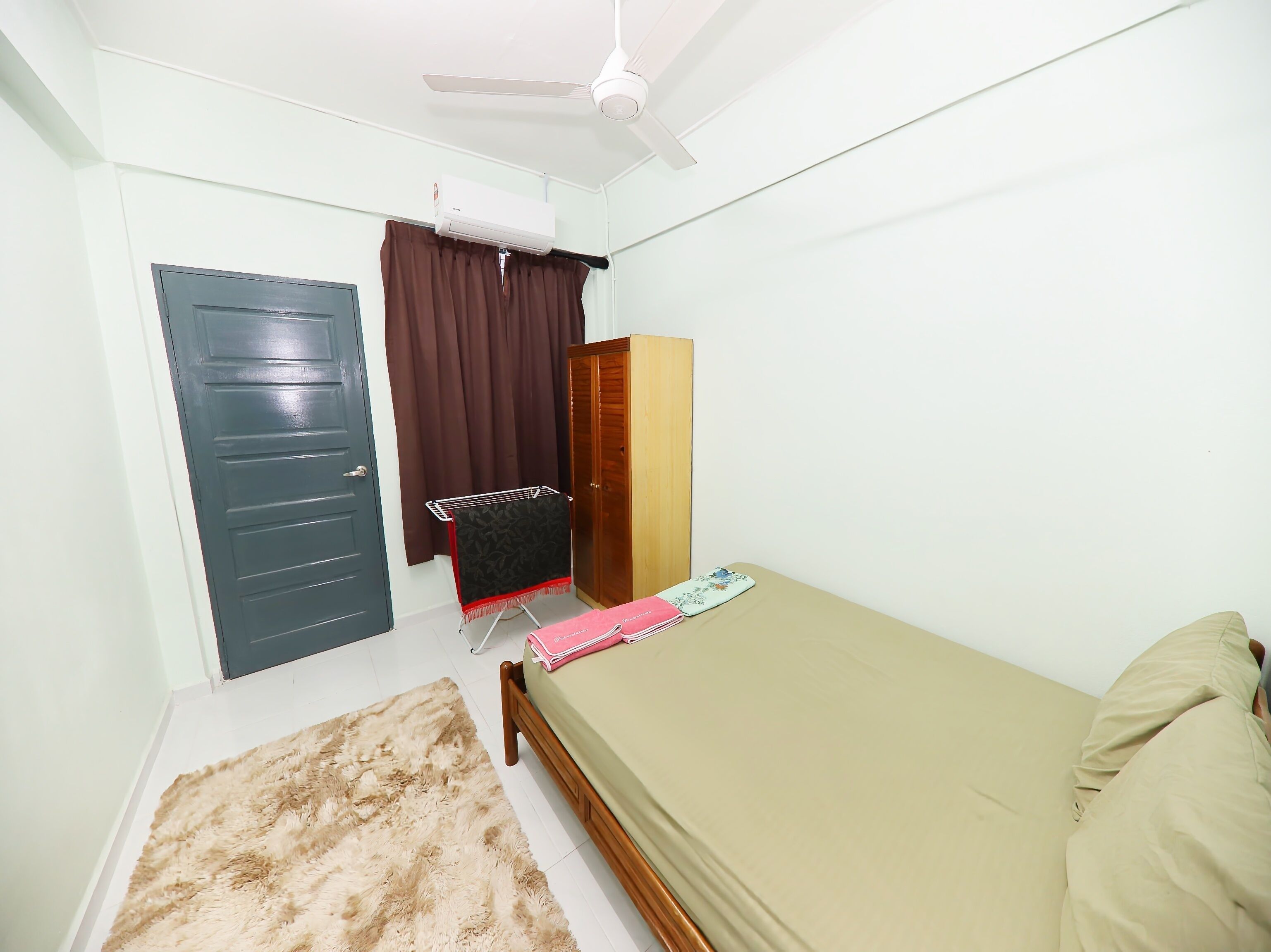 A bedroom with a bed, a wardrobe, a ceiling fan, an air conditioner, and a small table with a book.