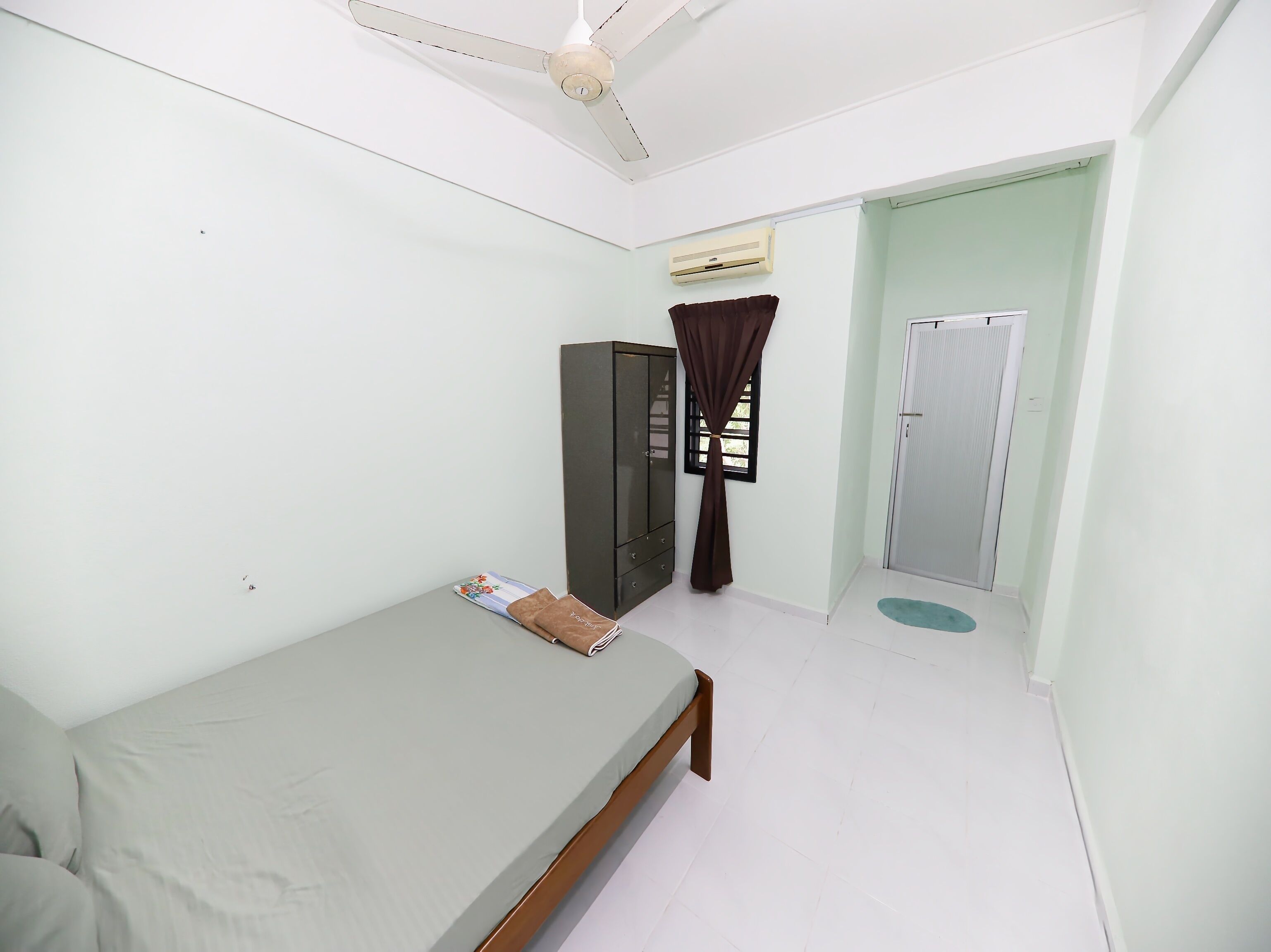 A small, clean room with a single bed, a wardrobe, a window with curtains, and a door.