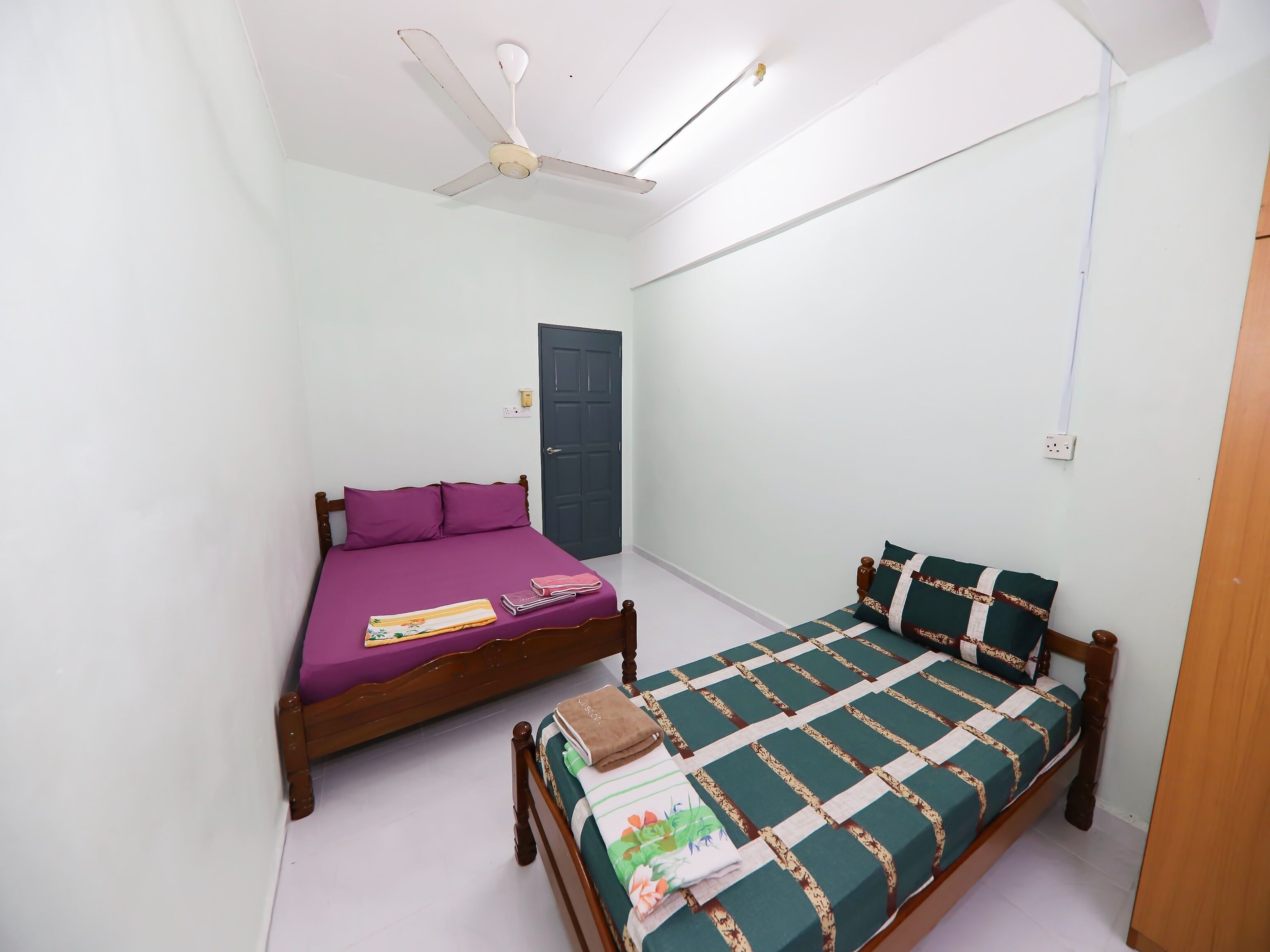 A bedroom with two beds, a ceiling fan, and a door.