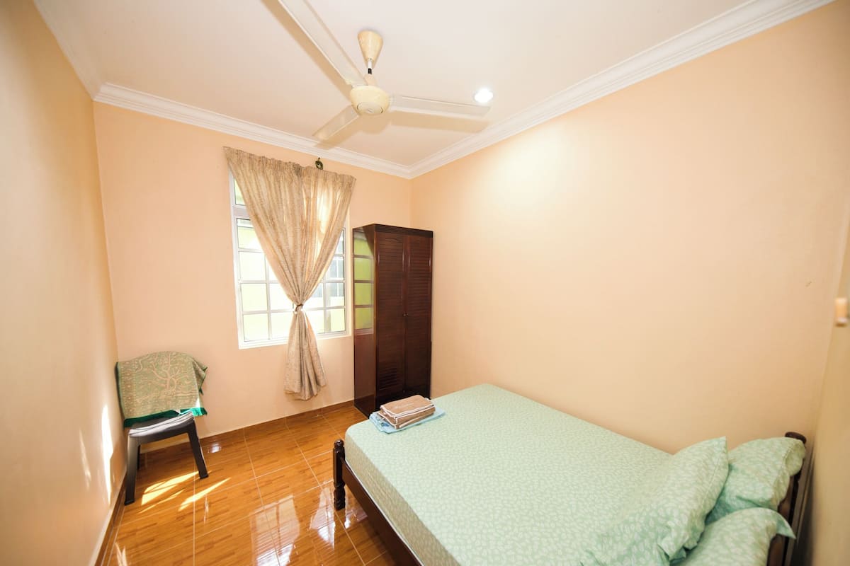 A bedroom with a bed, a wardrobe, a chair, and a ceiling fan.