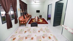 A room with a sofa set, a small table, a TV, and a bed with a purple bedspread.