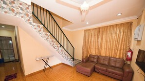 A living room with a wooden floor, a brown leather sofa, a staircase with a stone accent, and a ceiling fan.