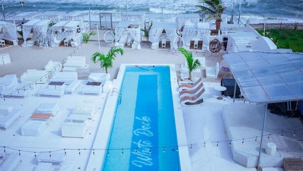 A pool area with lounge chairs and umbrellas, a blue pool, and a beach view. - WHITE DECK BEACH RESORT (Lekki)
