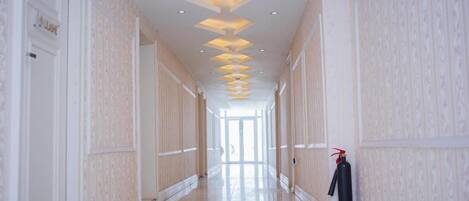 A long, well-lit hallway with patterned wallpaper and a fire extinguisher on the right.