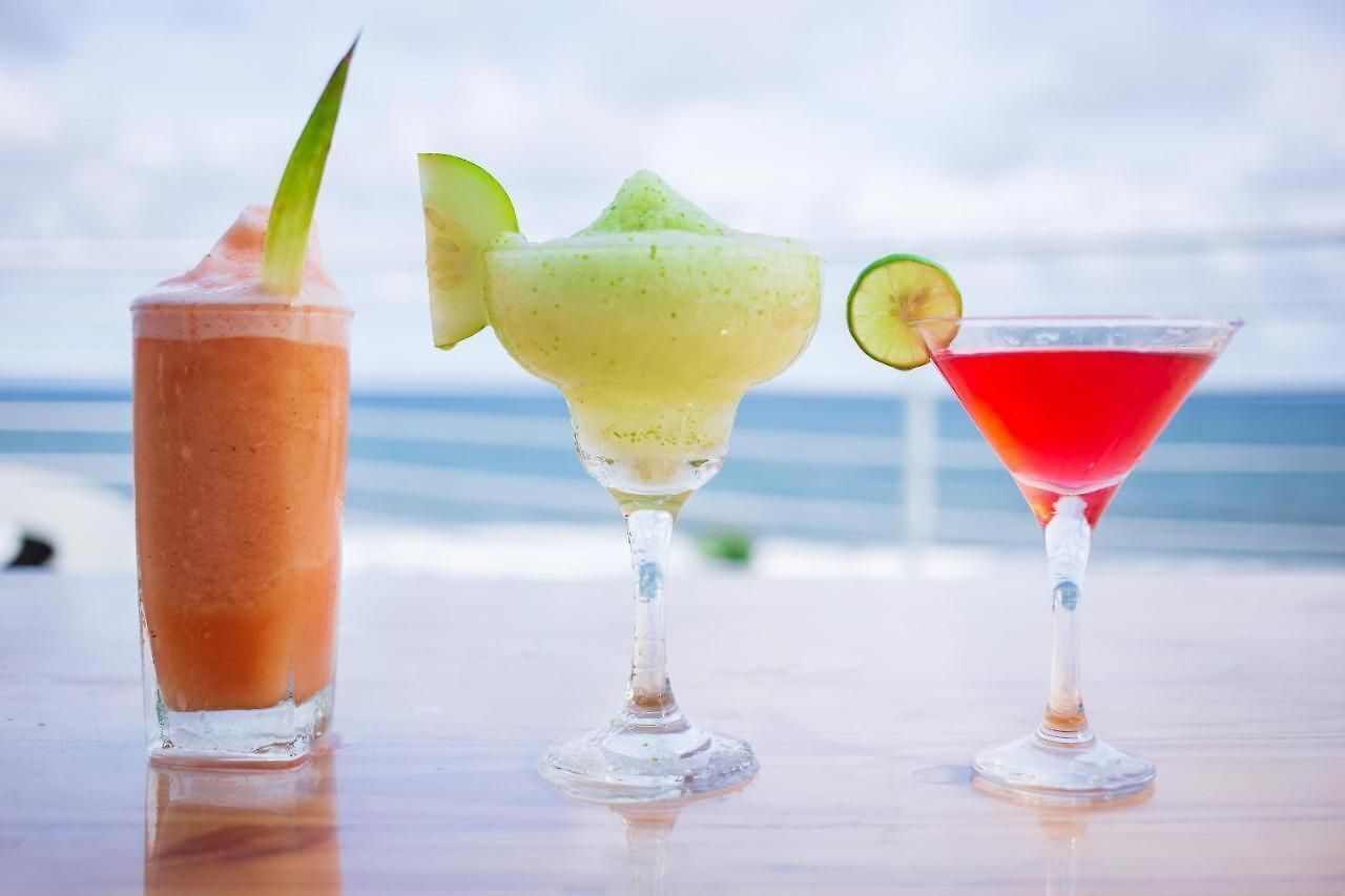 Three cocktails on a table with a beach view in the background.