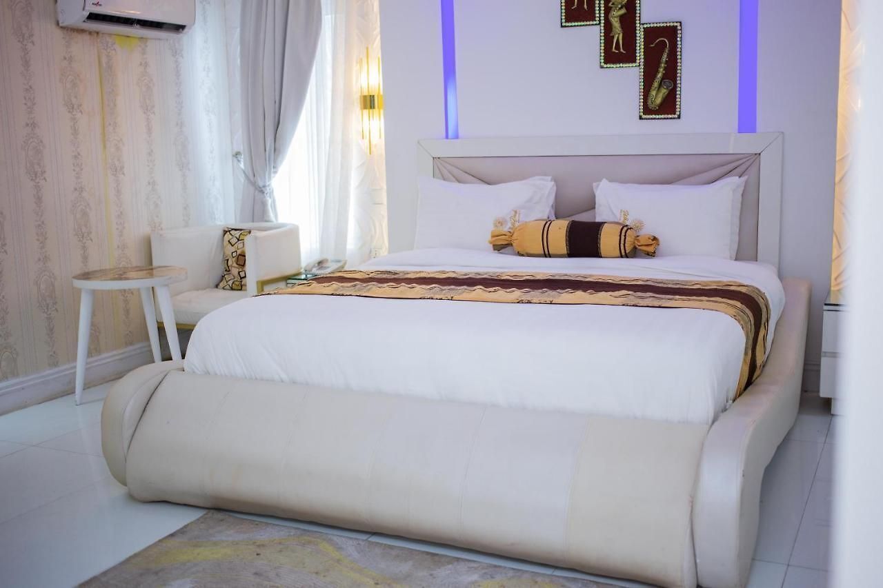 A bedroom with a large bed, a bedside table, a chair, and a wall-mounted air conditioner.