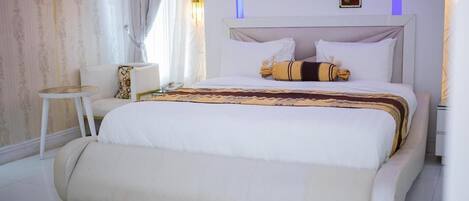 A bedroom with a large bed, a bedside table, a chair, and a wall-mounted air conditioner.
