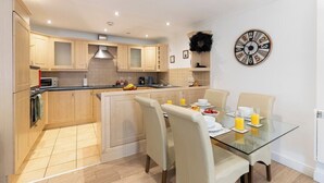 A modern kitchen with wooden cabinets, a glass dining table, and a clock on the wall.